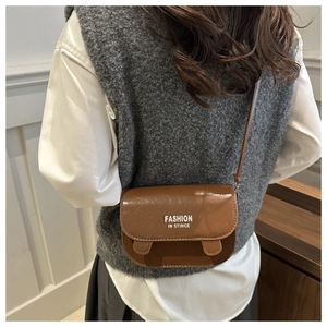 Détail d'un sac besace marron brillant avec texte Fashion porté par un mannequin