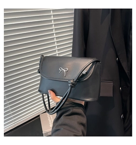 Detail of black leather crossbody bag featuring silver metallic bow and knotted strap