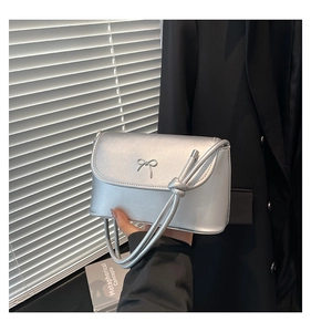 Close-up of a silver handbag featuring a metallic bow and stylish knotted shoulder strap