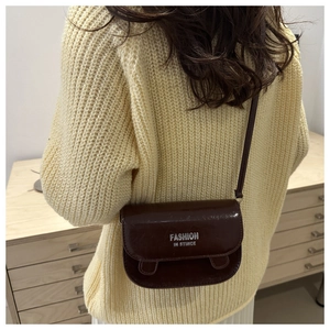 Détail du sac besace marron foncé avec logo argenté sur texture en cuir synthétique brillant