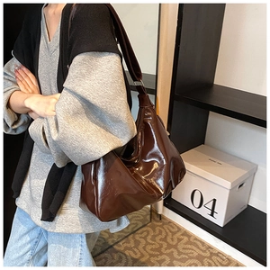 Detail of glossy dark brown patent leather tote bag styled on a female model