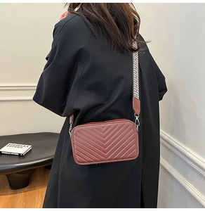 Sac bandoulière marron matelassé avec large sangle à motifs porté par un mannequin