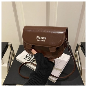 Détail d'un sac besace marron foncé brillant avec l'inscription blanche FASHION IN STINCE