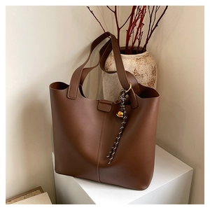 Detail view of large brown tote bag with vertical stitching and golden bell charm