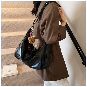 Detail of glossy black tote bag with plush bear charm worn by a model in a casual setting