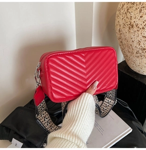 Gros plan détaillé d'un sac matelassé rouge avec surpiqûres en V et sangle tissée