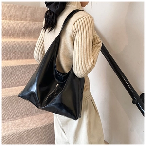 Minimalist large black shiny leather tote bag worn by a model in a modern interior