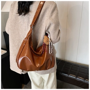 Macro detail of glossy brown leather tote bag with cute bear charm and woven rope