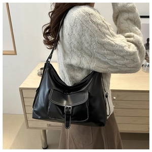 Detail of black leather crescent shoulder bag with white contrast stitching and buckle pocket