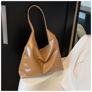 Close-up of caramel hobo bag in glossy leather texture leaning against a black door