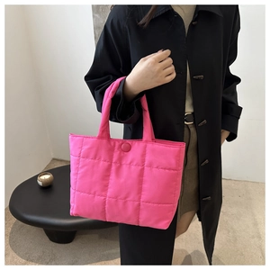 Detail of rose red quilted tote bag with square pattern and shoulder strap on model