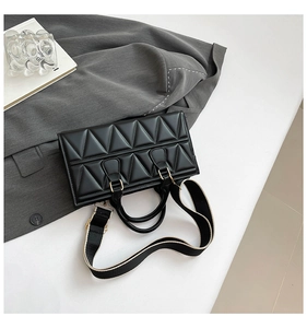 Detail of black triangular quilted handbag with wide fabric strap and golden hardware