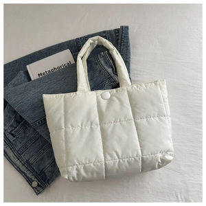 Detail of white quilted tote bag with magnetic clasp on denim and book background
