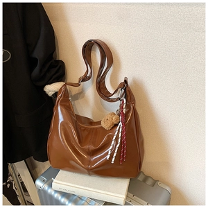 Brown glossy PU leather tote bag with a plush bear charm on white luggage background