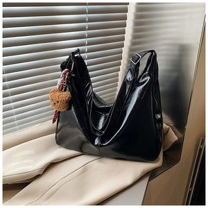 Detail of glossy black tote bag featuring a cute brown plush bear charm accessory