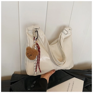 Detail of white glossy leather tote bag with a brown plush bear charm and striped rope