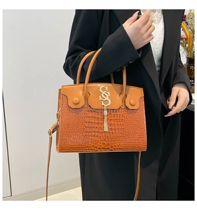 Détail du sac à main orange en cuir crocodile avec pendentif en métal doré en S