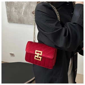 Close-up of red velvet shoulder bag with V-shaped quilting and golden chain strap