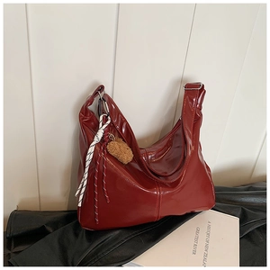 Detail view of burgundy patent leather tote with brown plush bear charm and woven cord decoration