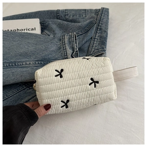 Détail d'une trousse de maquillage blanche matelassée avec broderie nœud noir et fermeture éclair