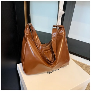 Detail of a large brown glossy leather tote bag with stylish metallic buckle and smooth zipper