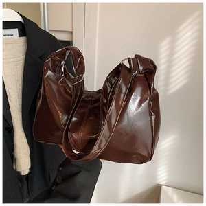 Detail of a deep brown glossy patent leather tote bag with silver hardware and soft folds