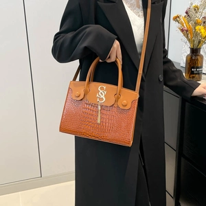 Sac à main marron motif crocodile avec pompon doré en forme de S dans un décor moderne