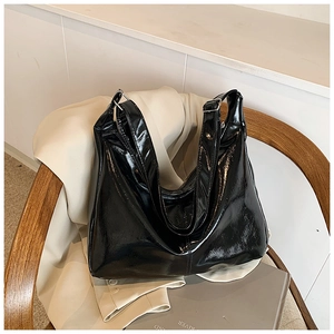 Minimalist large black glossy leather tote bag shown on a chair with aesthetic props