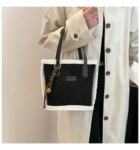 Detail of black fabric tote bag with white faux shearling trim and fashion label