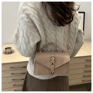 Sac bandoulière kaki avec boucle dorée, porté sur un pull en maille blanc élégant