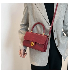 Detail view of burgundy leather handbag featuring a vintage gold circular twist lock