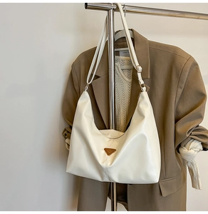 Detail of white half-moon hobo bag with a golden triangle logo on a suit background