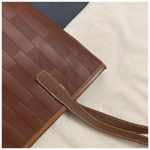Detail of woven brown leather tote bag showing contrast stitching and strap attachment