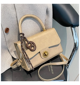 Detail of beige flap bag with gold ring lock, pretzel charm, and striped rope detail