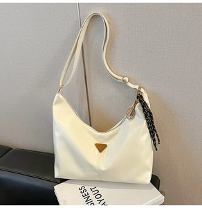Detail of cream white faux leather crescent bag with gold charm and silk scarf accent