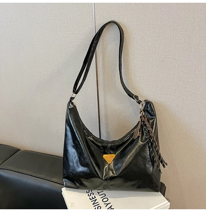 Close-up of glossy black Hobo tote with yellow triangle logo and woven fringe tassel