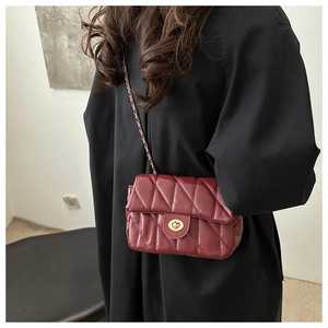 Detail of burgundy quilted crossbody bag featuring a golden twist lock and chain strap