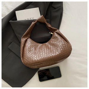 Detail of a brown woven faux leather shoulder bag with a stylish knotted handle design