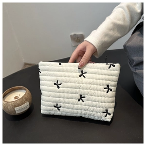 Detail der weißen gesteppten Kulturtasche mit schwarzen Schleifen und Reißverschluss