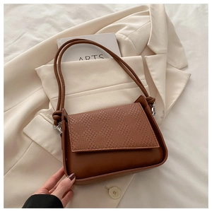 Detail of a brown leather crossbody bag featuring a textured woven flap and knotted strap