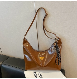 Detail of a brown glossy leather tote bag with black and white fringe and a tennis pendant