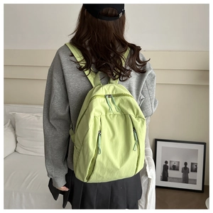 Zaino leggero in nylon verde con design multitasche, indossato da una modella in interni