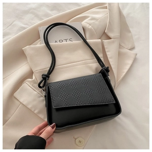 Close-up of black crossbody bag featuring woven texture flap and knotted strap detail