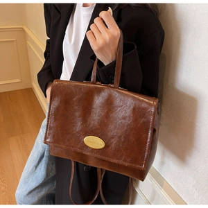 Detail of vintage brown oil wax leather backpack showing gold logo plate and carry handle