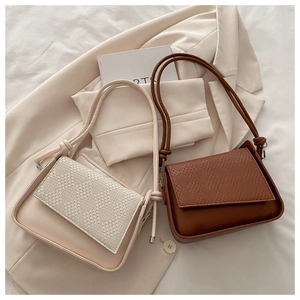 Close-up of woven texture flap and decorative knot on minimalist cream shoulder bag