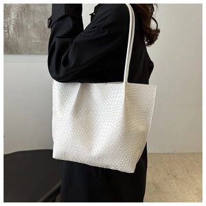 Detailed view of white woven texture leather tote bag worn by a model in black outfit