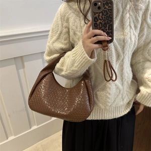Brown woven hobo bag with quilted pattern held by a model in a minimal interior