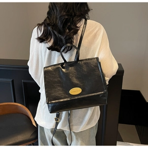 Detail of black vintage faux leather backpack with metallic oval logo and silver hardware