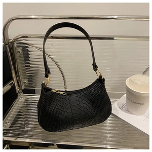 Close-up of black snakeskin texture shoulder bag with gold hardware on glass bench