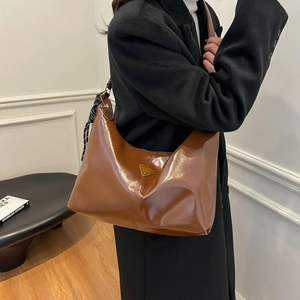 Brown patent leather tote bag with metallic logo and striped scarf accessory on shoulder
